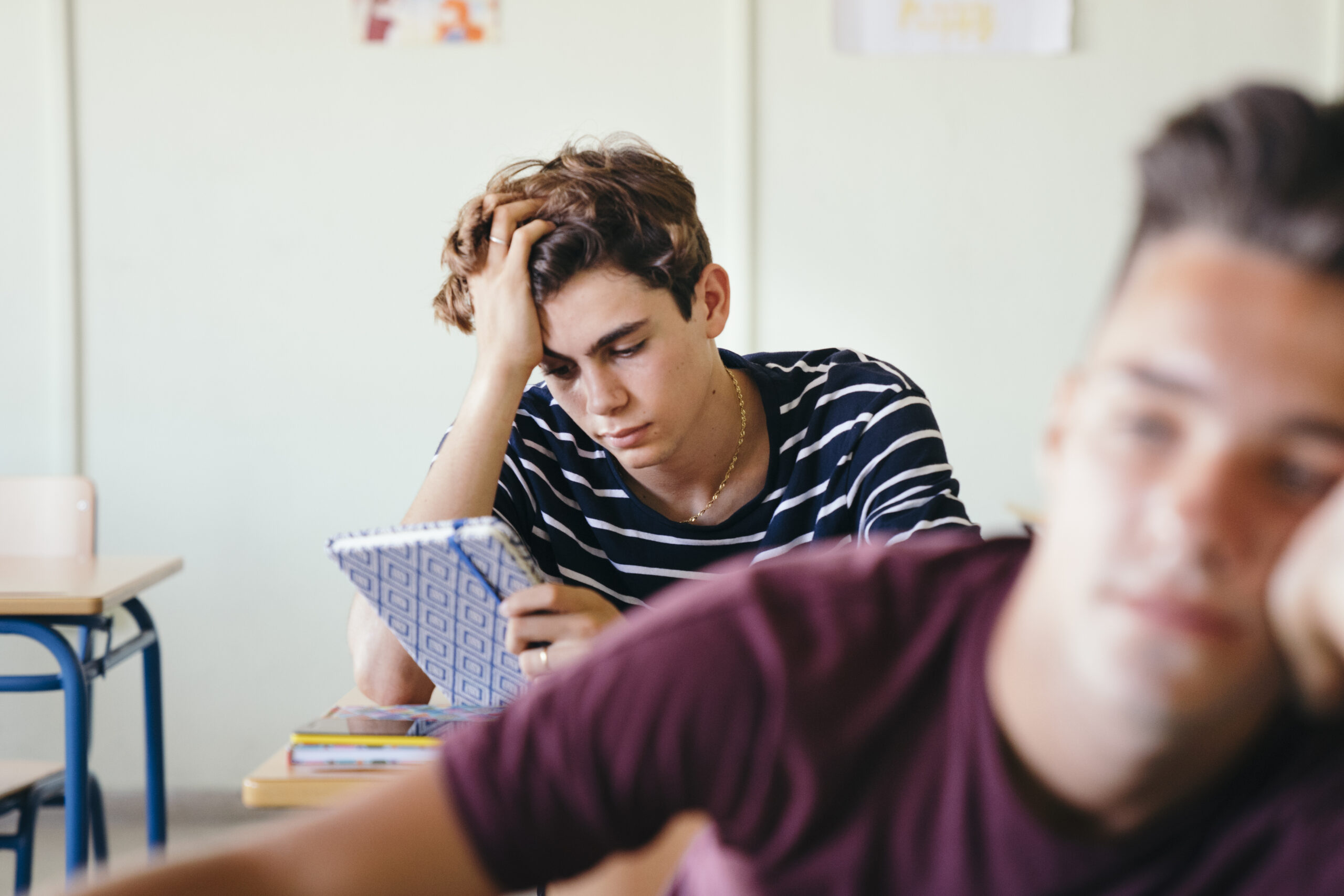 Un étudiants au fonds d'une salle de classe se tenant la tête en regardant un cachier